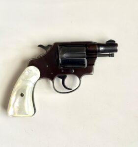 Brown-metal revolver with a white pearl grip lying on a light surface, side view showing cylinder and trigger guard.