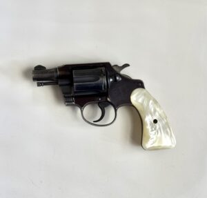 Revolver with a white pearl grip lying on a light surface, showing its cylinder and trigger.
