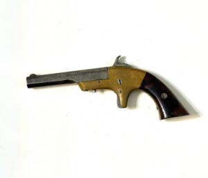 Partial view of a vintage revolver on a white surface, showing a brown grip and metal barrel with a hammer.